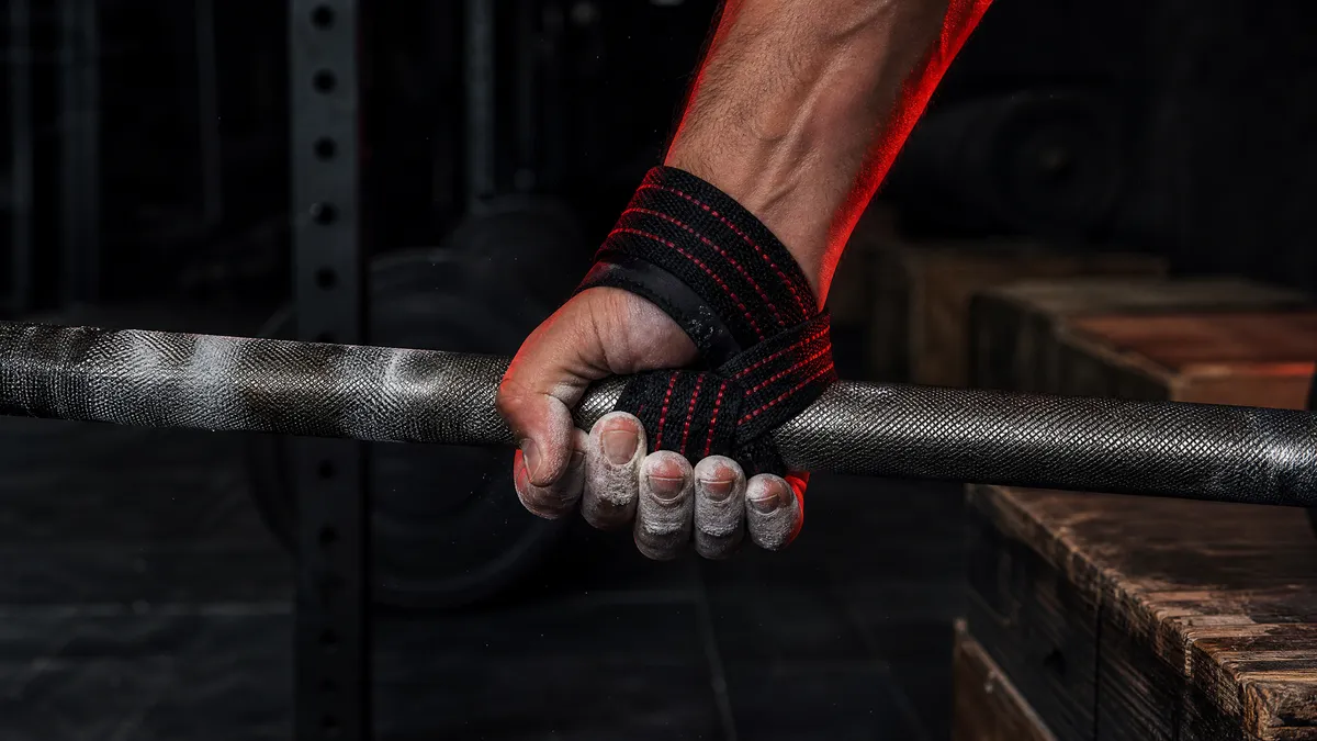 Close-up of a Might&Glory lifting strap wrapped under the bar and back toward the lifter
